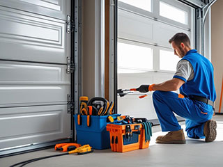 Technician performing inspection and maintenance on a residential garage door, with toolkits on the floor in Grayslake, IL.